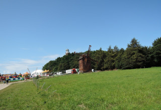 Campo verde con un molino de viento, árboles y una colorida zona de parque de atracciones al fondo.