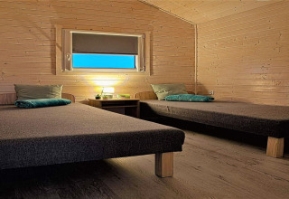 Wood-paneled room at Aquarius Cottages in Germany featuring two single beds and a cozy lamp.