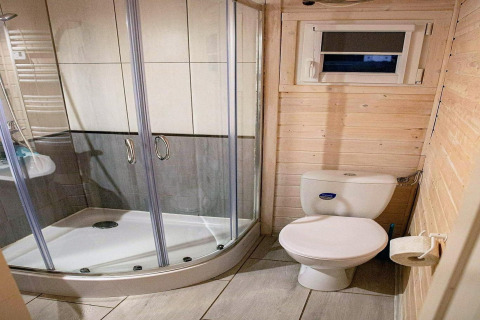 Badkamer met douchecabine, toilet en raam, houten wanden bij Aquarius Cottages, Duitsland.