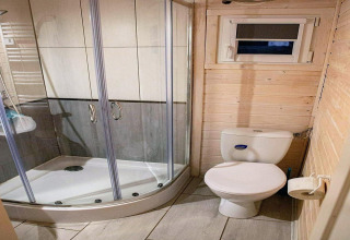 Badkamer met douchecabine, toilet en raam, houten wanden bij Aquarius Cottages, Duitsland.