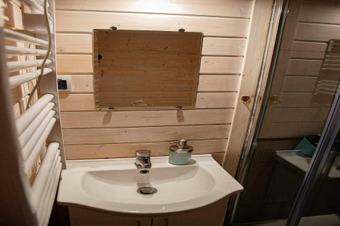 Badkamer met houten lambrisering, wastafel, lijstloze spiegel en zeepdispenser in Aquarius Cottages, Duitsland.