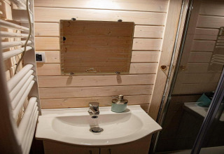 Badkamer met houten lambrisering, wastafel, lijstloze spiegel en zeepdispenser in Aquarius Cottages, Duitsland.