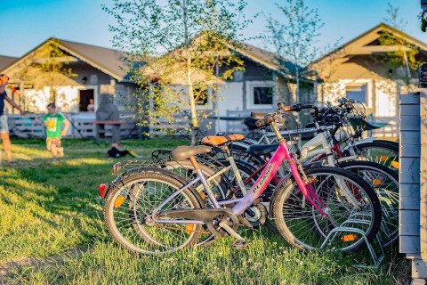 Bicycles parked on grass in front of Aquarius Cottages, children playing in background, sunny day in Germany.