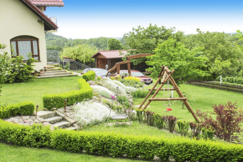 Tuin bij een lodge met groen gras, bloemperken, houten schommel en auto's geparkeerd op de achtergrond.