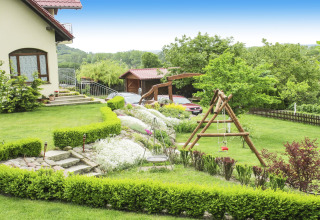 Tuin bij een lodge met groen gras, bloemperken, houten schommel en auto's geparkeerd op de achtergrond.