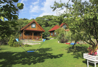 Sfeervolle houten huisjes op een heuvel met groene tuin en hangmat, zonnige dag in Duitsland.