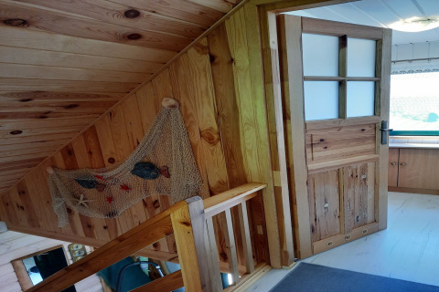 Houten trap met open deur, visnetdecoratie en houten lambrisering in een charmant Duits vakantiehuis.