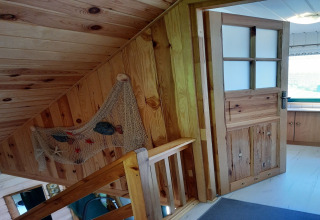 Houten trap met open deur, visnetdecoratie en houten lambrisering in een charmant Duits vakantiehuis.