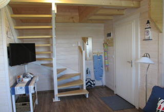 Ingang van lodge 'House on a hill' in Duitsland met trap, deur, tv en strijkplank in beeld.