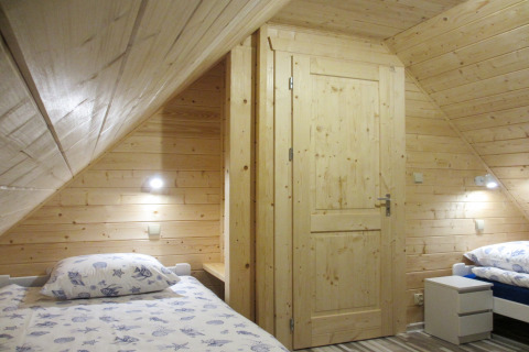 Houten slaapkamer met twee eenpersoonsbedden in lodge ‘House on a hill’ in Duitsland, sfeervol verlicht.