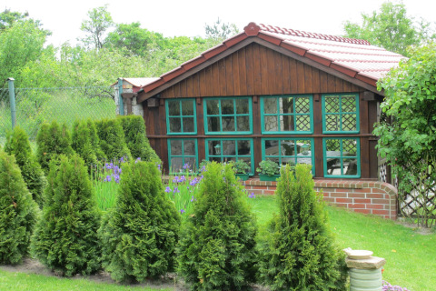 Gezellige houten lodge met groene ramen, omgeven door struiken en tuin bij House on a hill, Duitsland.