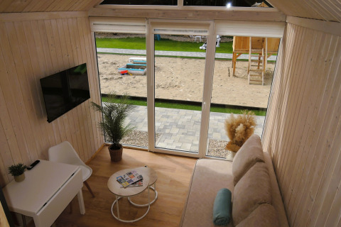Cabane moderne avec grandes fenêtres donnant sur une aire de jeux et un bac à sable, déco lumineuse.
