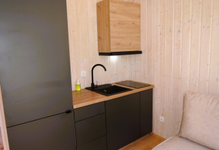 Pequeña cocina moderna con fregadero negro, encimera y paredes de madera en el interior de una cabaña.