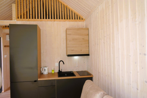 Pequeña cocina moderna en una cabaña de madera con armarios negros, hervidor y placas eléctricas.