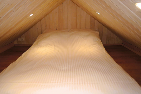 Knusse slaapruimte met schuin houten plafond en bed in de hut Turkusowa osada Wapnica.