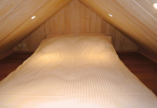 Knusse slaapruimte met schuin houten plafond en bed in de hut Turkusowa osada Wapnica.