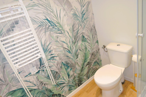 Baño con papel pintado de hojas tropicales, inodoro blanco y tendedero en Turkusowa osada Wapnica, Alemania.
