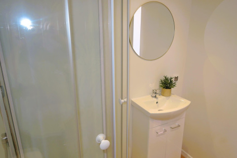 Moderne badkamer in 'Turkusowa osada Wapnica' met douchecabine, wastafel, ronde spiegel en plant.