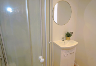 Moderne badkamer in 'Turkusowa osada Wapnica' met douchecabine, wastafel, ronde spiegel en plant.