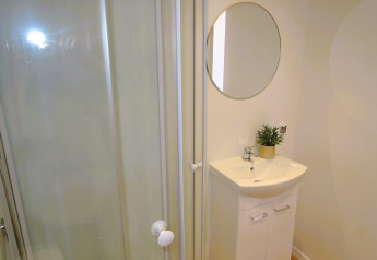 Baño moderno en 'Turkusowa osada Wapnica' con ducha, lavabo, espejo redondo y pequeña planta.