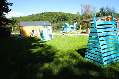 Parque infantil exterior con estructuras azules, césped y cabañas en Turkusowa osada Wapnica en Alemania.