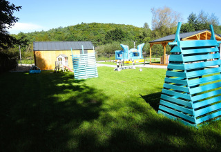Buitenspeeltuin met blauwe houten speeltoestellen, grasveld en hutten bij Turkusowa osada Wapnica in Duitsland.