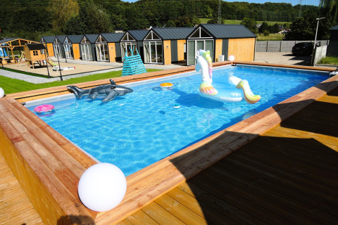 Piscina exterior con juguetes inflables frente a acogedoras cabañas de madera en Turkusowa osada Wapnica, Alemania.