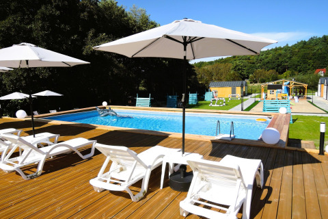 Piscina al aire libre con tumbonas y sombrillas blancas en una terraza de madera en Turkusowa osada Wapnica.