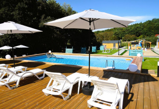 Piscina al aire libre con tumbonas y sombrillas blancas en una terraza de madera en Turkusowa osada Wapnica.