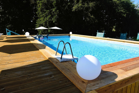Piscina al aire libre con terraza de madera y tumbonas en Turkusowa osada Wapnica, rodeada de árboles verdes.