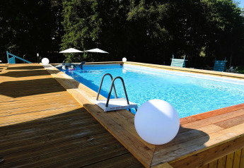 Udendørs swimmingpool med træterrasse og liggestole ved Turkusowa osada Wapnica, omgivet af grønne træer.