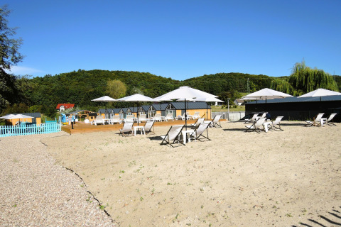 Buitenzandgebied bij Turkusowa osada Wapnica met ligstoelen, parasols en groene heuvels op de achtergrond.