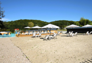 Buitenzandgebied bij Turkusowa osada Wapnica met ligstoelen, parasols en groene heuvels op de achtergrond.