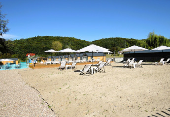 Udendørs strandområde ved Turkusowa osada Wapnica, med liggestole, parasoller og grønne bakker.