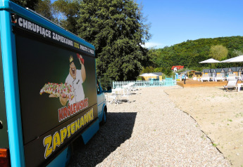Foodtruck mit Zapiekanki-Werbung, neben Kiesweg und Strandliegen bei Turkusowa osada Wapnica, Polen.