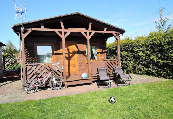 Knus houten huisje voor vier personen, met veranda, ligstoelen, fiets en ballen in een zonnige tuin.