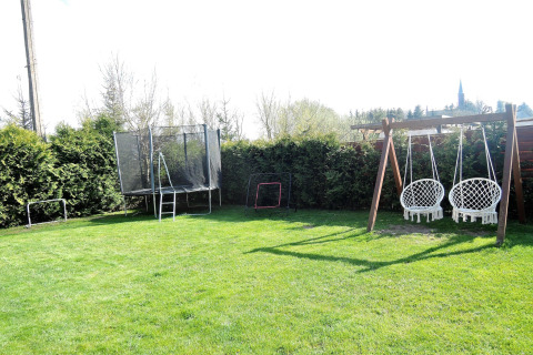 Garten an einer Hütte mit Schaukeln, Trampolin und Fußballtoren; grüne Hecken und Bäume im Hintergrund.