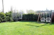 Giardino di una baita con altalene, trampolino e porte da calcio; siepi e alberi verdi sullo sfondo.