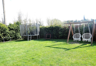 Giardino di una baita con altalene, trampolino e porte da calcio; siepi e alberi verdi sullo sfondo.