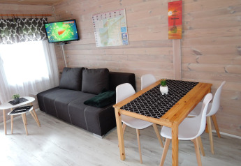 Woonkamer in een Duitse hut met zwarte bank, eettafel voor vier, witte stoelen en een TV aan de muur.