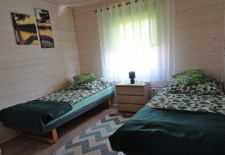 Zwei Einzelbetten mit grüner Bettwäsche in einem hellen Holzzimmer mit Nachttisch und Gardinen in einer Hütte.