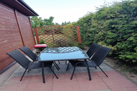 Outdoor patio with six black chairs and a glass table at a cottage in Germany, surrounded by greenery.