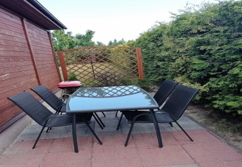 Terrasse mit sechs schwarzen Stühlen und Glastisch an einer Hütte in Deutschland, von Grün umgeben.