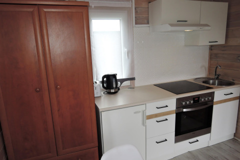 Keukengedeelte in een Duits huisje met fornuis, oven, kast, zwarte waterkoker en houten wand bij raam.