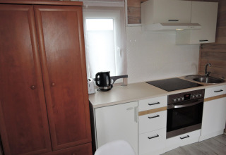 Keukenzone in een Duitse chalet met kookplaat, oven, kast, zwarte waterkoker en houten wandbekleding.