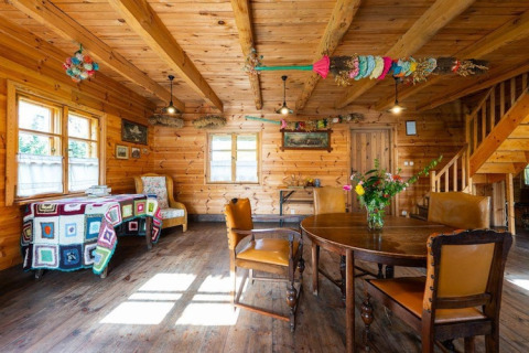 Knus houten lodge-interieur met eettafel, kleurrijke decoraties en veel daglicht door ramen.