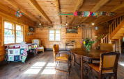 Knus houten lodge-interieur met eettafel, kleurrijke decoraties en veel daglicht door ramen.