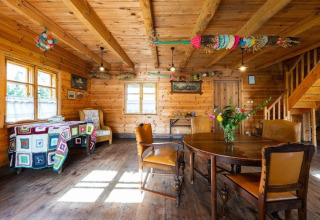 Gezellig interieur van houten lodge met eettafel, kleurrijke versiering en veel lichtinval via ramen.