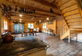 Knusse blokhut met houten interieur, oude kachel, eettafel, blauwe kast en houten trap.