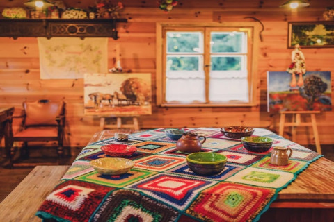 Interno di un rifugio in legno con tovaglia colorata all'uncinetto, ciotole di ceramica e quadri vivaci.